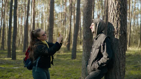 Girl Takes a Picture of a Guy on the Phone in the Forest