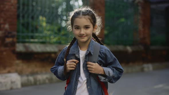 Portrait of Little Schoolgirl Standing on School Yard Holding Bag Turn Around and Looking at Camera