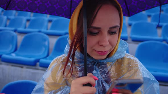 A focused woman in a hoodie and a plastic raincoat using a mobile phone