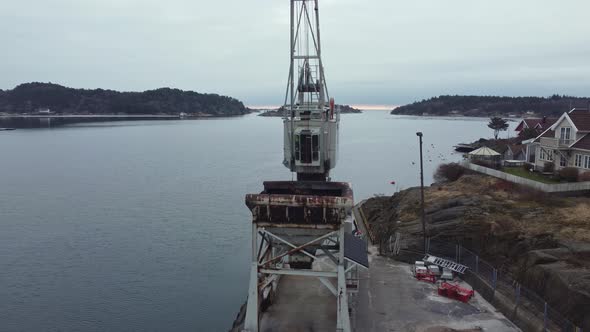 Old rusty harbor crane in Lillesand Norway - Aerial rotating around crane wit grab and north sea in