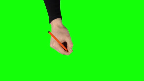 Male Hand in a Black Sweater with Orange Pencil Is Writing on Green Screen Background. Close Up