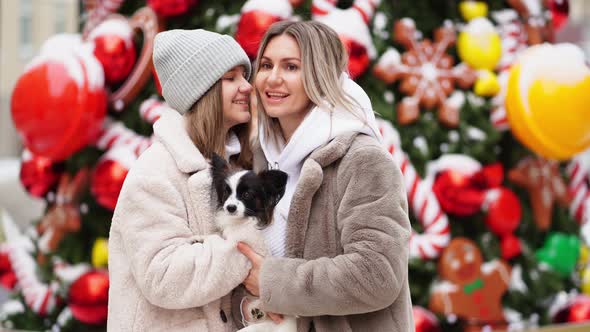 Mom and Daughter with Dog Papillon Near Christmas Tree on Street
