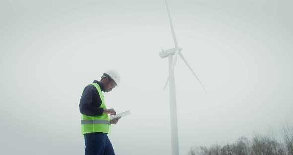 A Man in a Work Uniform is Diagnosing a Wind Turbine Using a Digital Tablet