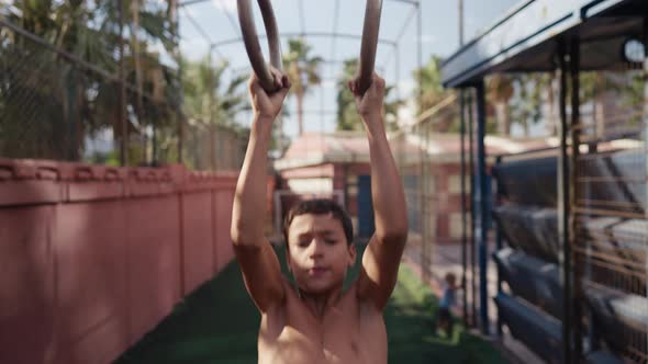 Young Athletic Boy Doing Exercise on the Gymnastic Rings at Street Workout Place