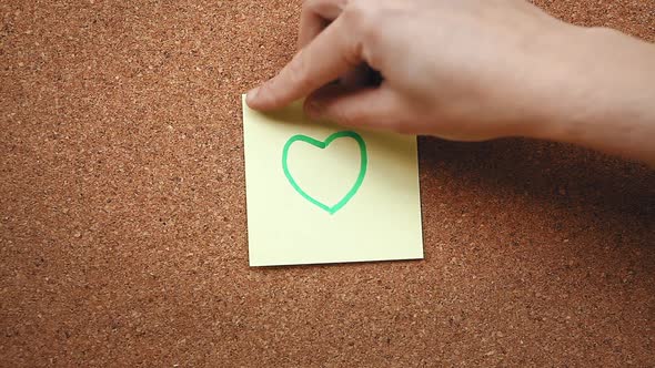 Person sticking a heart note on a cork board