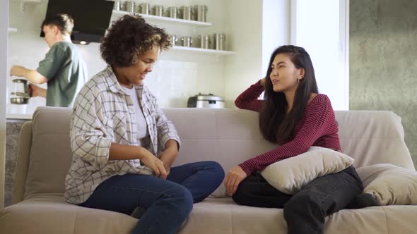 Two Girlfriends an AfricanAmerican and an Asian Chatting with Each Other While Sitting at Home on