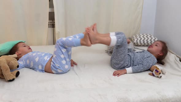 Two Smiling Preschool Toddler Children In Pajamas Playing With Teddy Bear on Bed