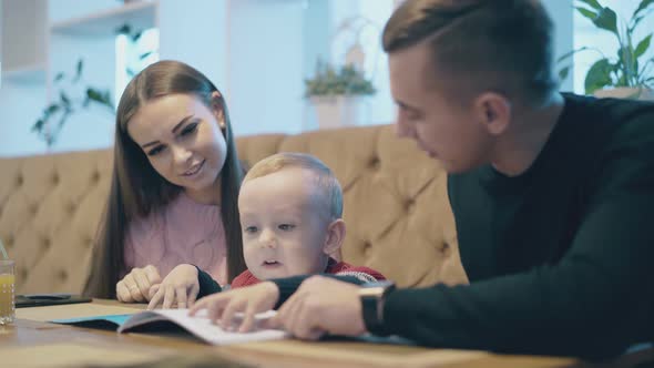Happy Family with Young Boy in Pullover Looks at Menu Book