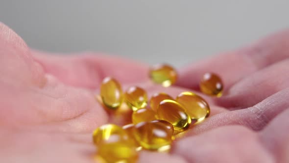 Yellow Omega 3 capsules in palm. Wrinkled dry skin. Macro