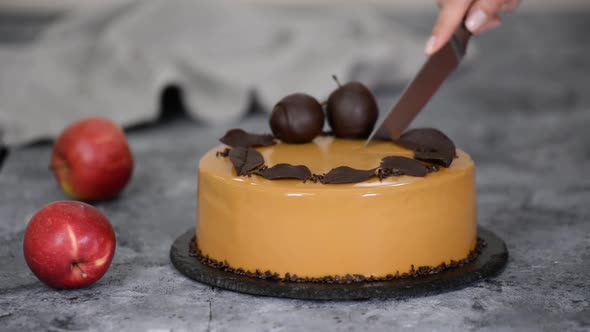 Female hands cutting a caramel apple mousse cake with mirror glaze. Autumn cake.French food