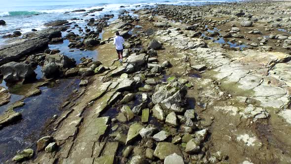 Tracking shot of a young man running on a rocky ocean beach shoreline