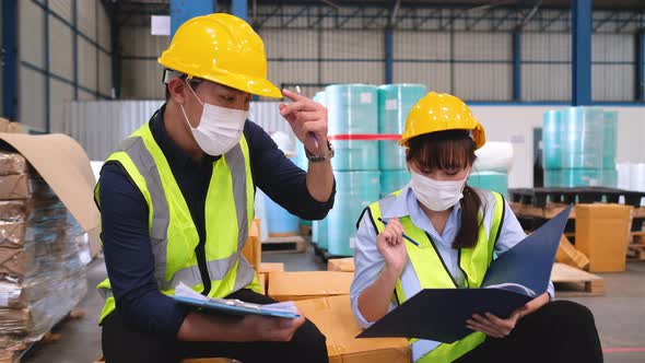Warehouse or factory workers man and woman with hygiene mask sit on box and talk together