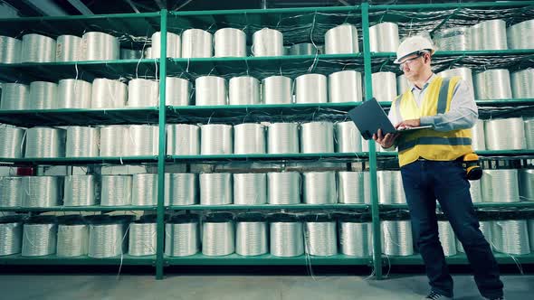 Male Worker with a Laptop is Observing Rolls of Fiberglass