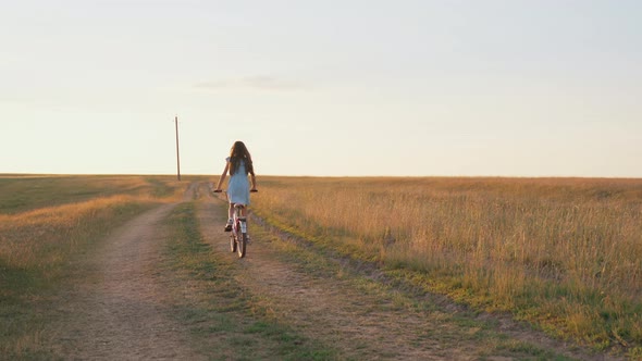 A little girl riding a bike on a country road. A girl rides a small bike across the field at sunset.