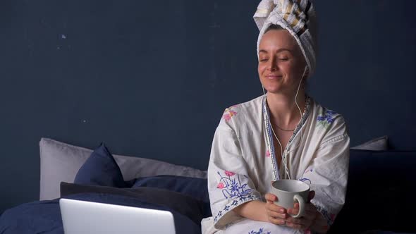 Woman Relax on Bed Wearing Towel on Head and Moving to Music in Earphones Akspb