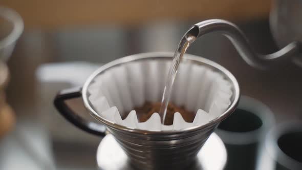 Slow motion kettle pouring hot water over freshly ground coffee beans in filter paper