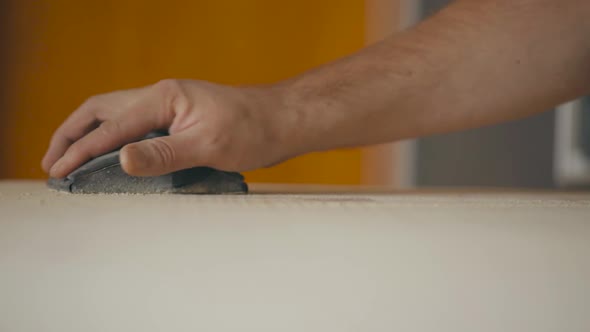 slow motion static shot of a man sanding a table with a sanding block