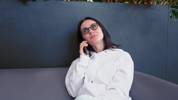 Smiling Young Business Woman of European Appearance in a White Sweater Sits in a Cozy Green Place in