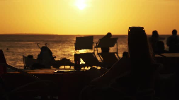 Silhouette Young Woman Sitting at Table on Beach and Looking at Sunset By Ocean