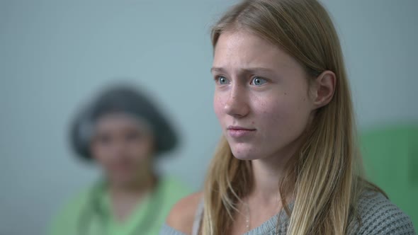 Closeup Face of Scared Teenage Girl Looking Back at Blurred Doctor Looking Away Shaking Head