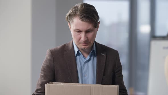 Portrait of Sad Frustrated Caucasian Brunette Man Holding Cardboard Box Indoors