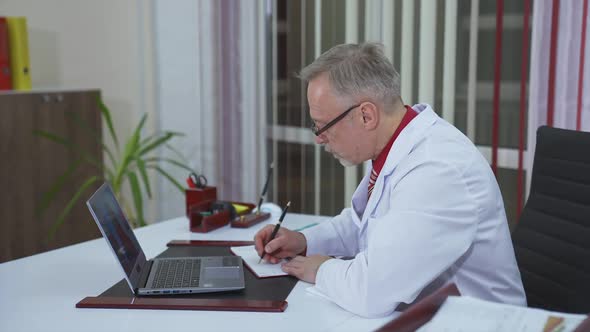 Doctor chatting with patients online, using laptop at his workplace. Telemedicine concept