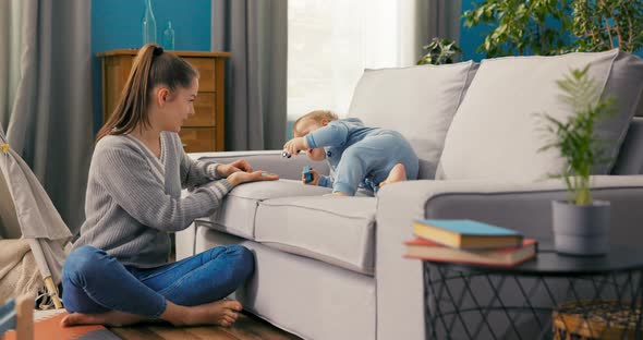 Joyful Full of Strength Child is Sitting on Couch in a Blue Bodysuit Playing with