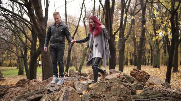 Romantic Young Couple Walking on the Rocks in Autumn Park During the Day Holding Hands