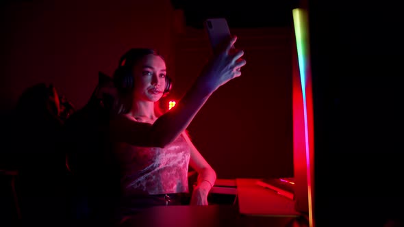 Tattooed Young Woman Sitting in Neon Gaming Club and Taking a Selfie on Her Phone