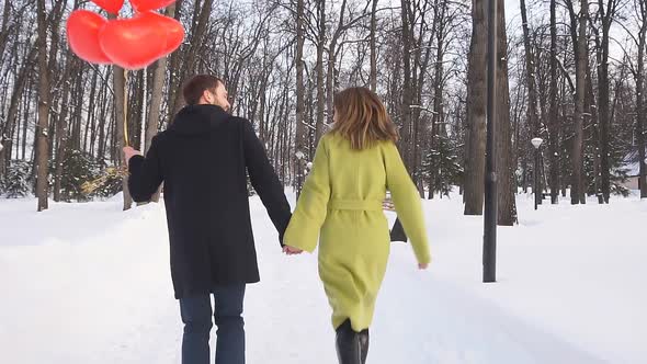 Romantic Couple in Love with Red Balloons Runs Through the Park on a Winter Day and Enjoys Time