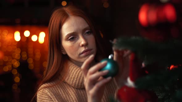 Close-up Face of Sad Redhead Young Woman Decorating Christmas Tree Alone at Cozy Living Room
