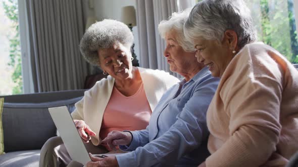 Three diverse senior women using laptop together sitting on the couch at at home