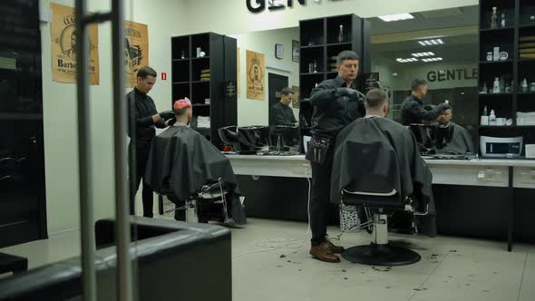 Two Experienced Masters in Black Gloves Make Haircuts to Customer in Barbershop