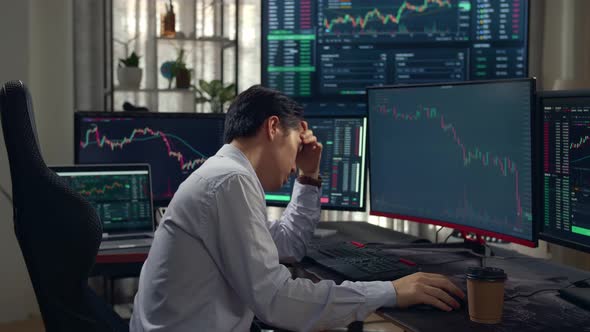 Disappointed Of Asian Male Stock Market Broker Analyzing Graphs On Multiple Computer Screens