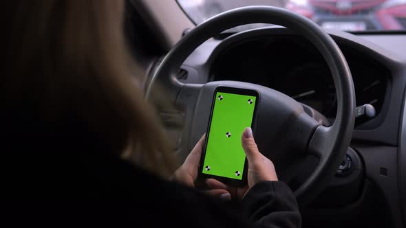 A Woman is Driving a Car with a Phone in Her Hands a Chroma Key on the Screen