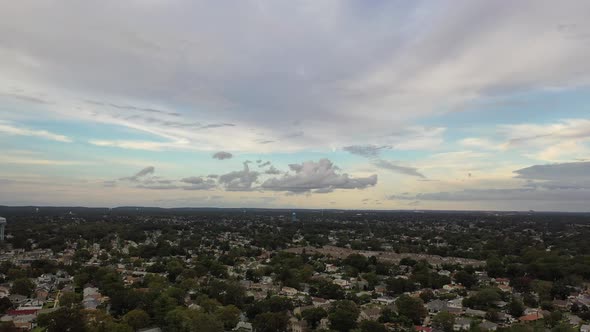 An aerial view of a quiet suburban neighborhood on Long Island. It is a cloudy day. The sky is beaut