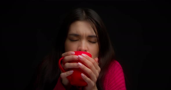 Brunette in a Pink Sweater is Frozen and Warms Up with a Hot Drink in a Red Mug