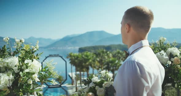 Groom on wedding ceremony with flowers waiting for bride against mountain