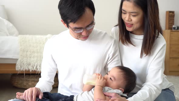 Asian Family of Young Father and Mother Feeding a Baby Boy From Milk Bottle