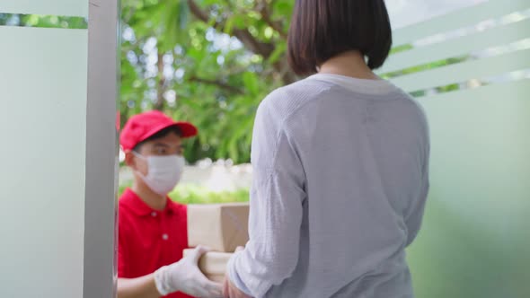 Asian deliver man wearing face mask in red uniform handling package boxes to young woman customer.