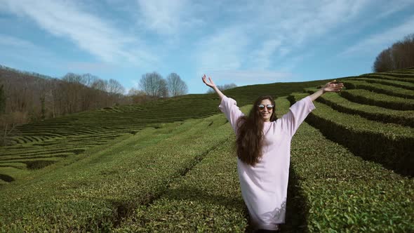 Young Woman Raises Her Arms Up Against a Background of Tea Bushes