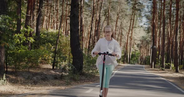 Blonde Child is Riding a Scooter in the Park