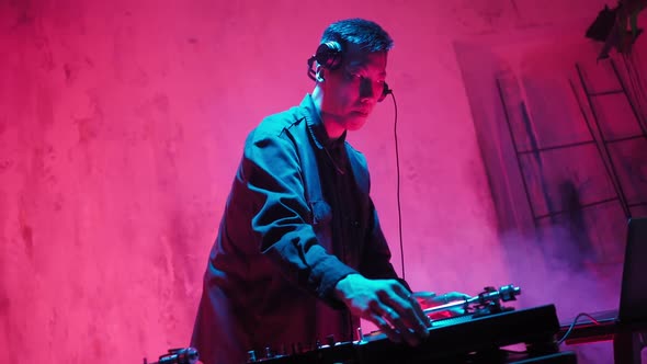Modern DJ of Asian Appearance Performs a Music Track in Neon Lighting