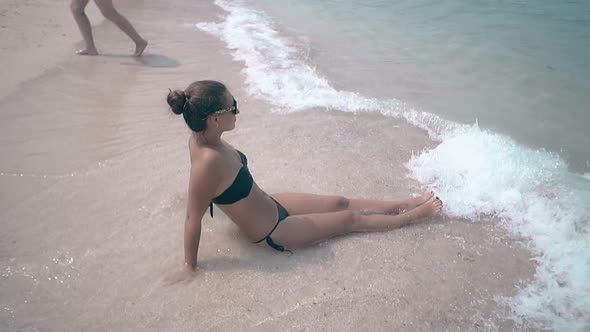 Woman Walks on Beach Near Girl Lying Among Rolling Waves