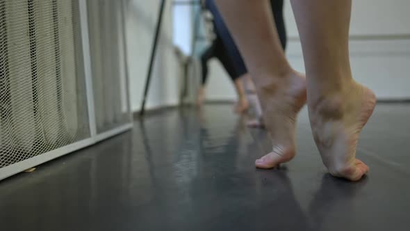 Barefoot Legs of Young Caucasian Slim Woman Rehearsing at Dance Barre with Unrecognizable Friends