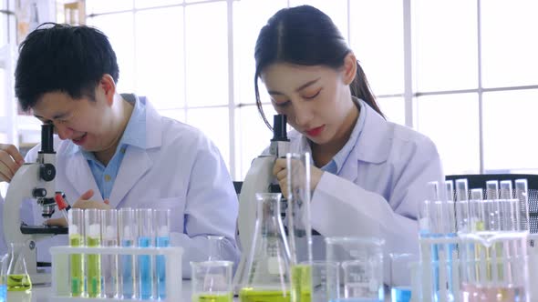 Young Asian Female Scientist Doing Research in Laboratory Wearing Lab Coat and Gloves with Colleague