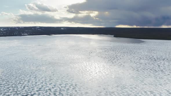 Drone Flying Above Frozen Lake with Melting Ice Shield and Clouds Reflection