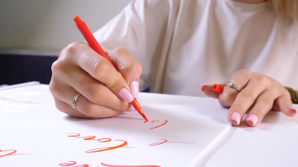 Calligrapher student practices in writing word LOVE with red marker on canvas. 