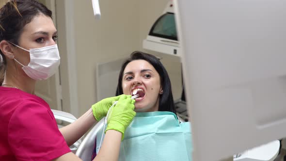 Young Female Dentist Examining the Mouth of a Patient with an Intraoral Camera and Showing Image on