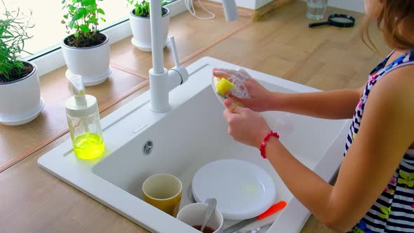 The Child Washes the Dishes in the Kitchen